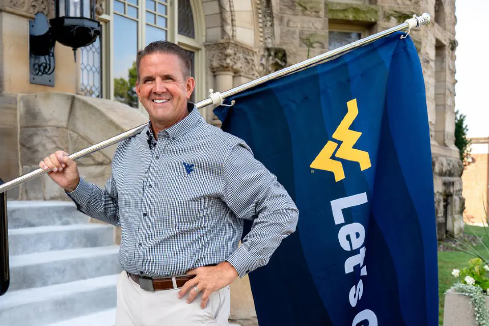 WVU President Benson holding a "Let's Go" flag in front of Stewart Hall on WVU's downtown campus